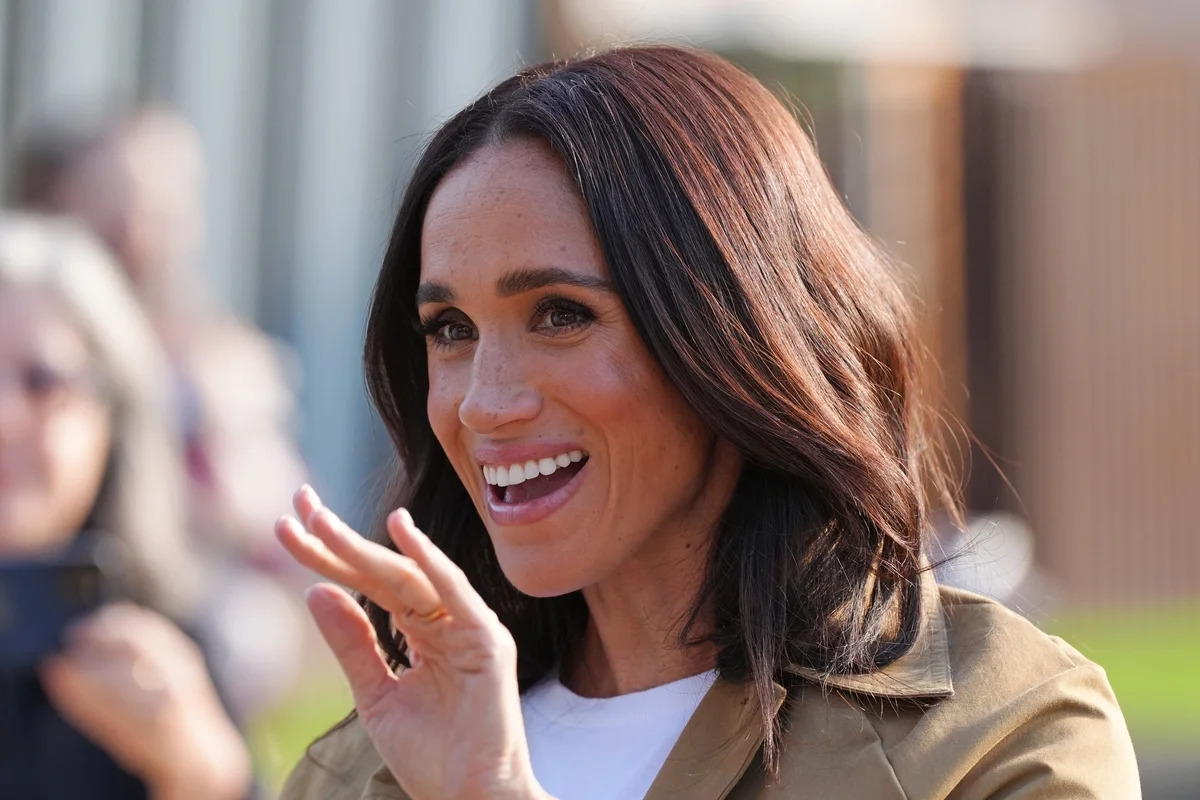 Foto colorida de mulher com cabelo castanho-escuro acenando - Meghan Markle - Metrópoles