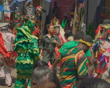 Gugu Mbatha-Raw's character walks through a crowded street festival with people in colourful costumes