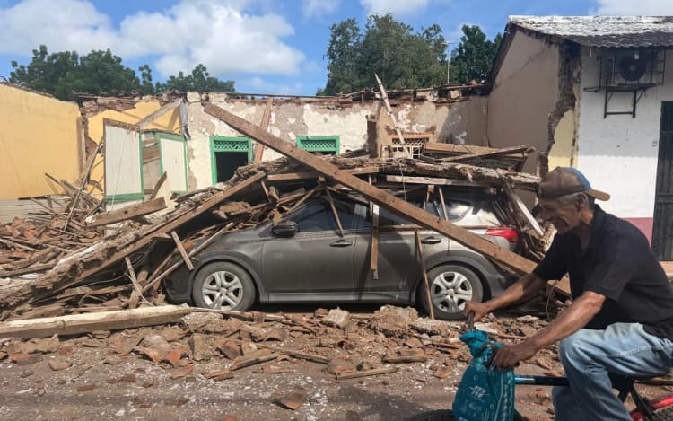 A man rides a bicycle past a collapsed house and a car buried under debris in the town of Chitre, about 250 km southwest of Panama City, on October 10, 2026. A powerful 7.7-magnitude earthquake rocked Panama on October 10, 2026, collapsing buildings and roads in the center of the country and injuring at least 27 people, with no deaths reported. (Photo by DANIEL DE CARTERET / AFP)