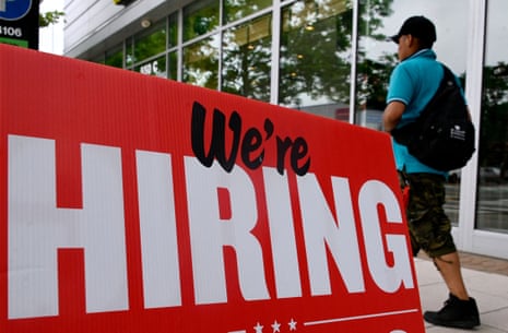 A close-up of a red "We're Hiring" sign outside a restaurant, with a man walking past